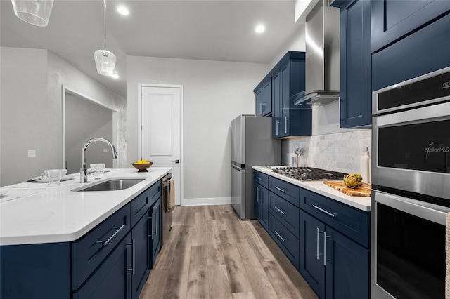 kitchen featuring a sink, blue cabinetry, wall chimney range hood, and appliances with stainless steel finishes