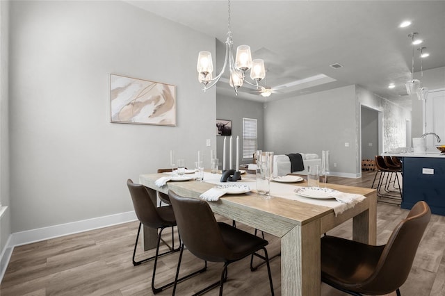 dining space featuring baseboards, light wood-style floors, a chandelier, a raised ceiling, and recessed lighting
