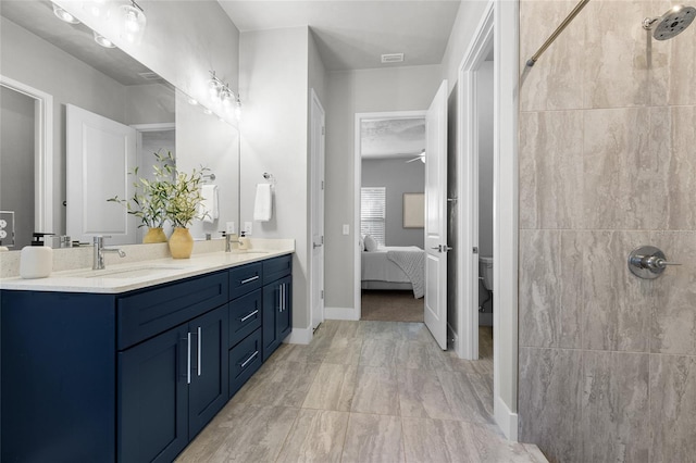 full bathroom with double vanity, toilet, a ceiling fan, baseboards, and tiled shower
