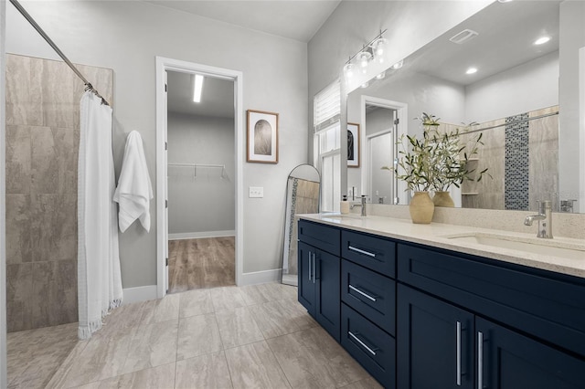 bathroom with tiled shower, double vanity, a walk in closet, and baseboards