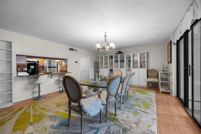 dining area featuring a chandelier, light wood-style flooring, and a textured ceiling