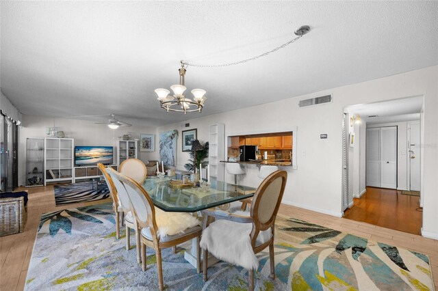 dining space featuring a chandelier, a ceiling fan, wood finished floors, baseboards, and a textured ceiling