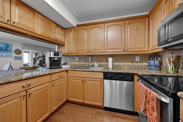kitchen with appliances with stainless steel finishes, a sink, light stone countertops, light wood-style flooring, and backsplash