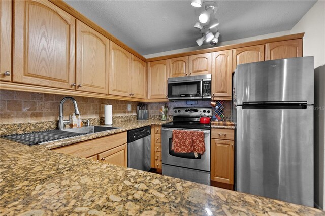 kitchen with stainless steel appliances, a sink, backsplash, light brown cabinetry, and light stone counters