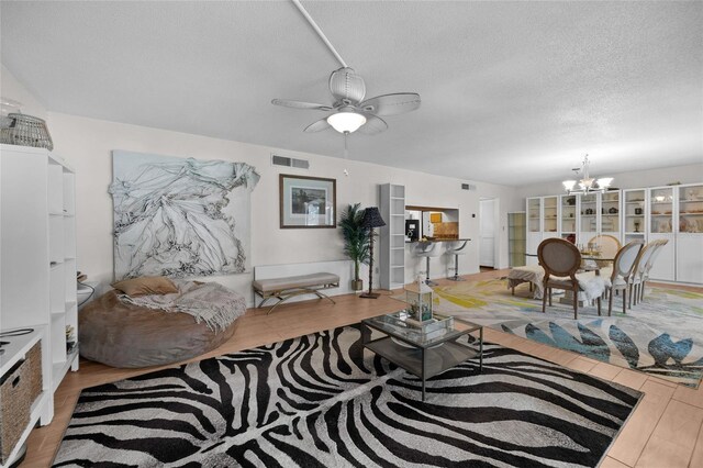 living area with a chandelier, a textured ceiling, a ceiling fan, and wood finished floors