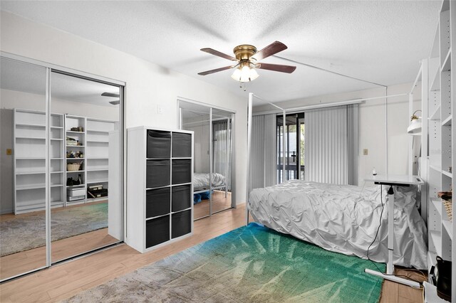 bedroom featuring wood finished floors, a textured ceiling, two closets, and a ceiling fan