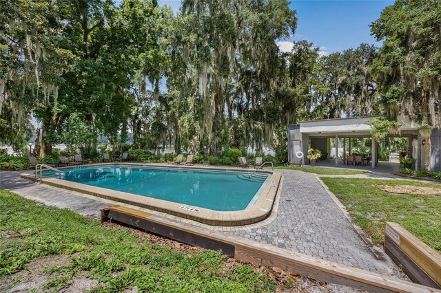 community pool with a patio, a lawn, and view of scattered trees