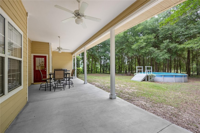 view of patio / terrace featuring a ceiling fan, outdoor dining area, an outdoor pool, and view of wooded area