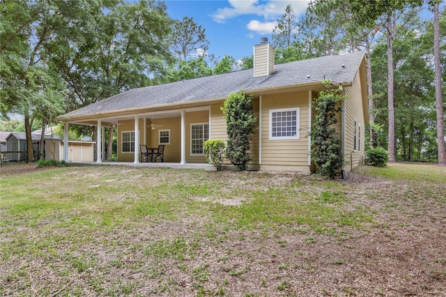 rear view of property featuring a shed, ceiling fan, an outbuilding, a chimney, and a yard