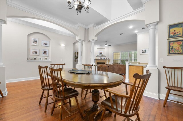 dining area with ornate columns, wood finished floors, crown molding, arched walkways, and baseboards