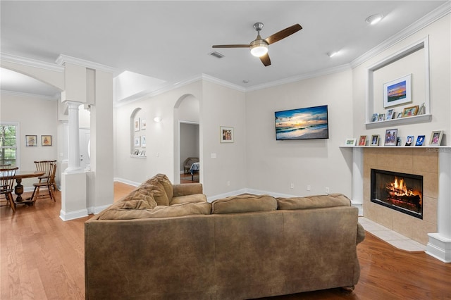 living room with wood finished floors, ceiling fan, ornamental molding, a tile fireplace, and arched walkways
