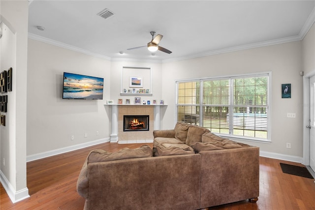 living area with a ceiling fan, wood finished floors, a fireplace, crown molding, and baseboards