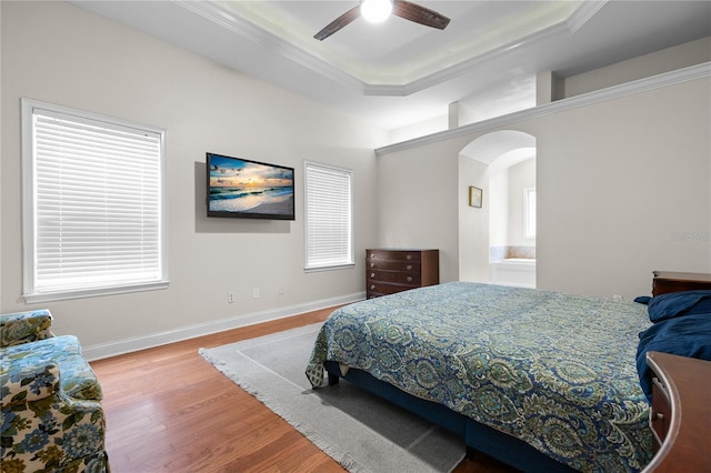 bedroom with a tray ceiling, wood finished floors, arched walkways, crown molding, and ceiling fan