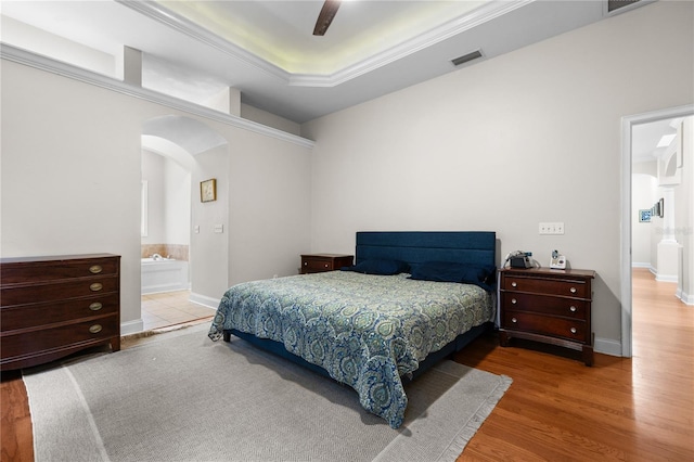 bedroom featuring arched walkways, wood finished floors, a ceiling fan, and connected bathroom