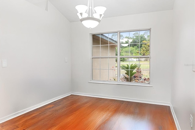 spare room with a chandelier, wood finished floors, and baseboards