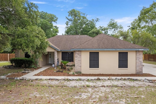 ranch-style home featuring fence, a shingled roof, and stucco siding