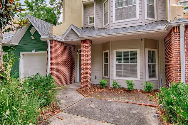 entrance to property with brick siding, a garage, and a shingled roof