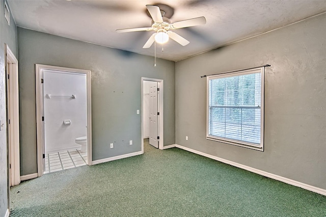 unfurnished bedroom with carpet, a spacious closet, connected bathroom, a ceiling fan, and baseboards