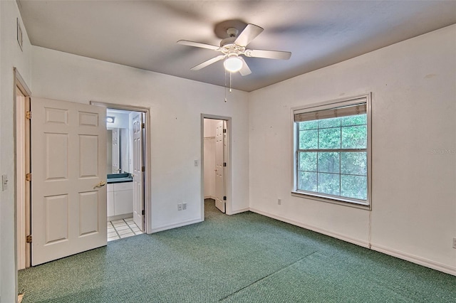 unfurnished bedroom with carpet, a walk in closet, baseboards, ensuite bath, and a ceiling fan
