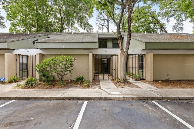 view of exterior entry featuring uncovered parking, a gate, a shingled roof, and stucco siding