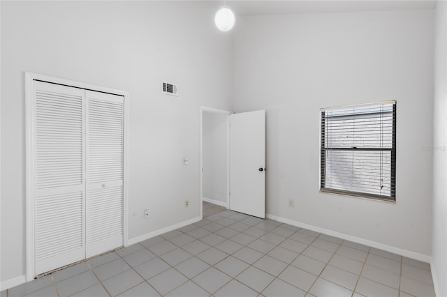 unfurnished bedroom featuring a high ceiling, a closet, baseboards, and light tile patterned floors