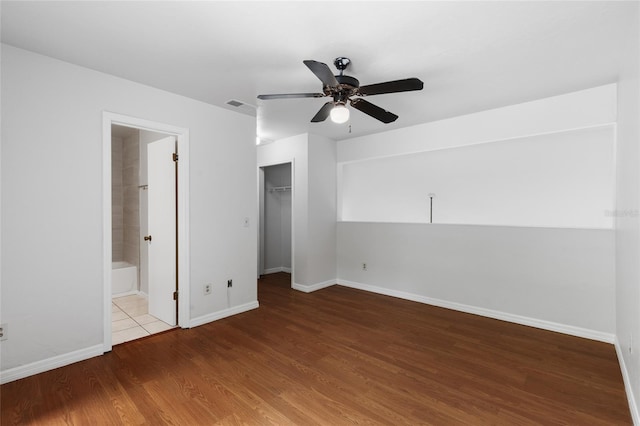 unfurnished bedroom with wood finished floors, a closet, baseboards, a ceiling fan, and a walk in closet