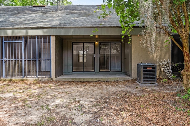 property entrance with a shingled roof, central AC, and stucco siding