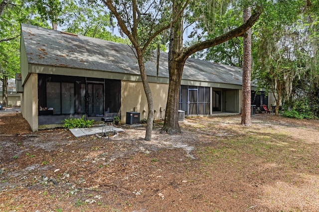 rear view of house with a sunroom, central AC unit, and stucco siding