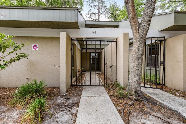 entrance to property featuring a gate, stucco siding, and fence