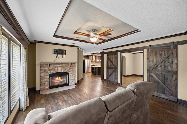 living area with a barn door, a tray ceiling, wood finished floors, baseboards, and ornamental molding