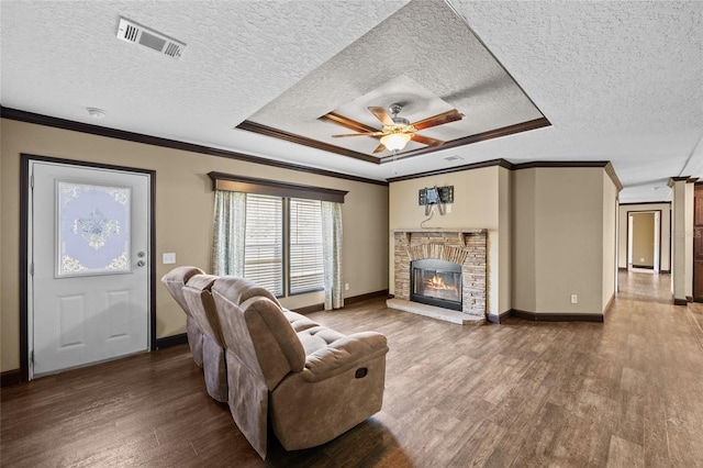 living area featuring ornamental molding, wood finished floors, a ceiling fan, a textured ceiling, and a stone fireplace