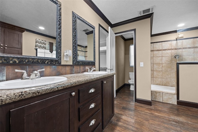 bathroom with ornamental molding, toilet, a tile shower, wood finished floors, and double vanity