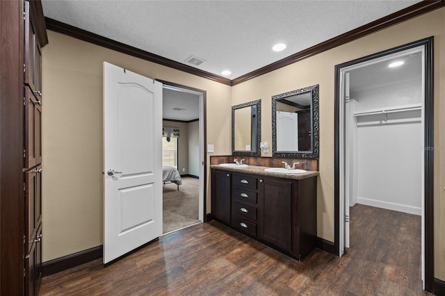 bathroom with wood finished floors, ornamental molding, double vanity, baseboards, and recessed lighting