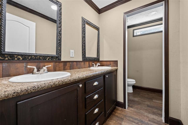 bathroom with crown molding, wood finished floors, toilet, double vanity, and baseboards