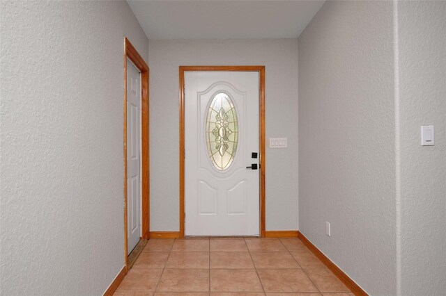 entryway featuring light tile patterned flooring, a textured wall, and baseboards
