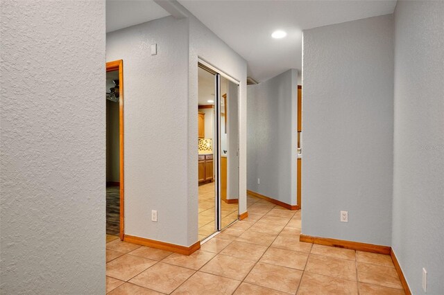 hall with a textured wall, baseboards, and light tile patterned floors