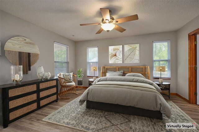 bedroom featuring multiple windows, wood finished floors, a textured ceiling, baseboards, and ceiling fan
