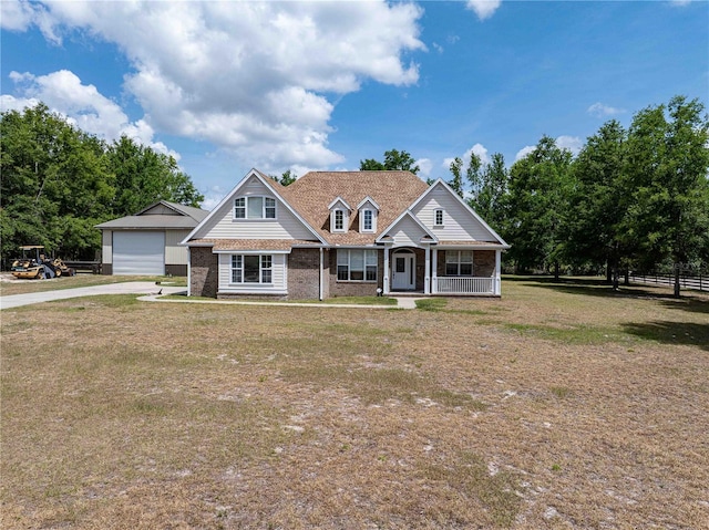 view of front facade with concrete driveway, covered porch, brick siding, a detached garage, and a front yard