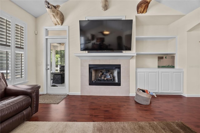 living room featuring wood finished floors, a tile fireplace, vaulted ceiling, baseboards, and built in shelves
