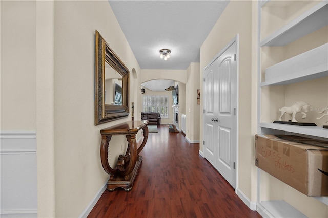 hall with dark wood-type flooring, arched walkways, and baseboards