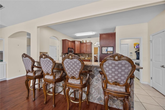 dining space with arched walkways, baseboards, and light wood finished floors