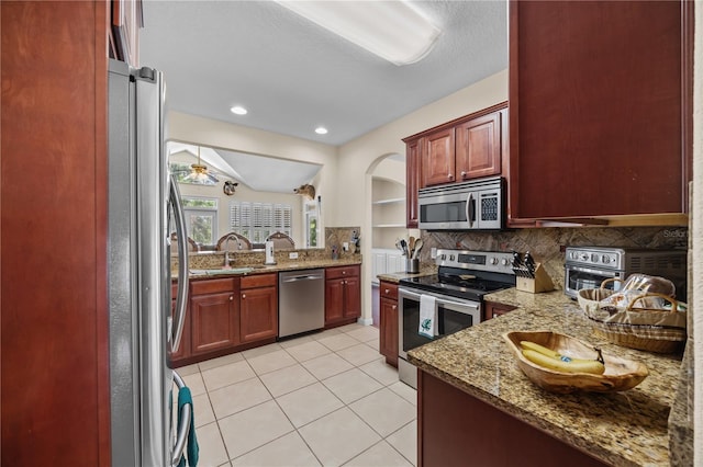 kitchen with appliances with stainless steel finishes, a sink, decorative backsplash, dark brown cabinets, and light stone countertops