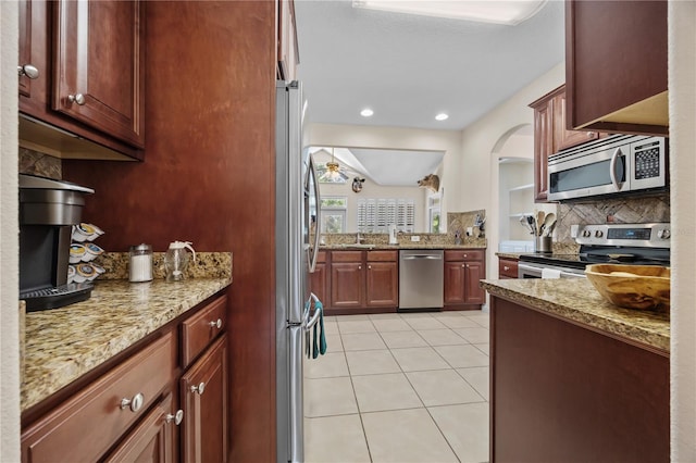 kitchen with appliances with stainless steel finishes, decorative backsplash, light tile patterned floors, and light stone counters
