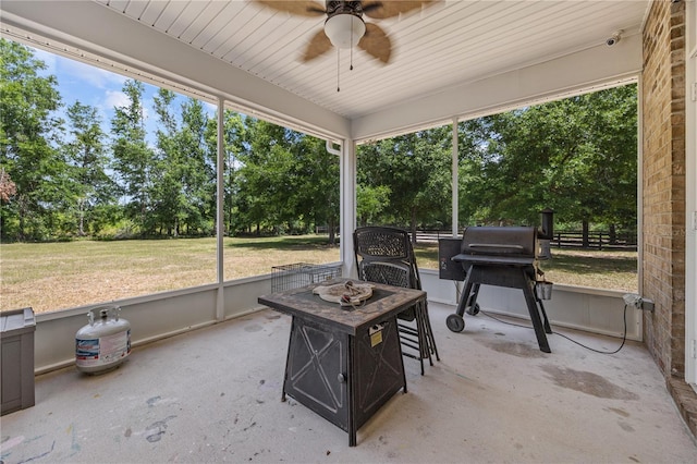 sunroom featuring a ceiling fan, view of wooded area, and healthy amount of natural light