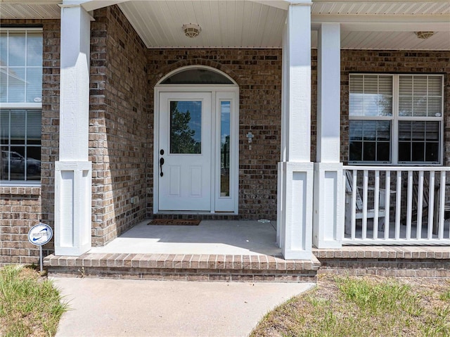 doorway to property featuring a porch and brick siding