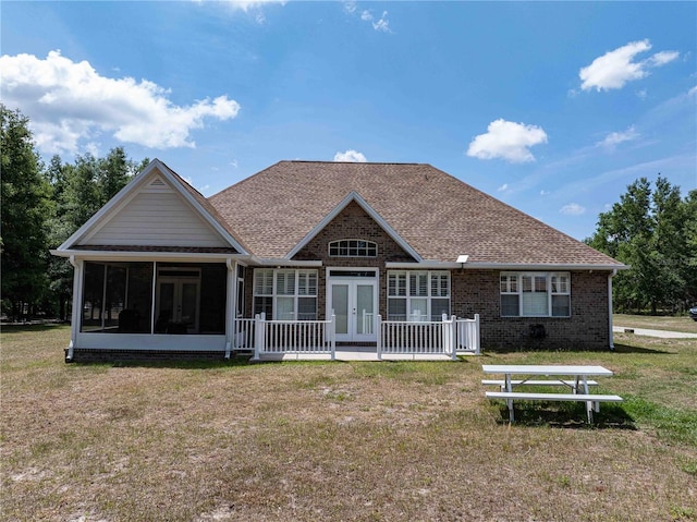 rear view of property featuring french doors, a sunroom, a lawn, roof with shingles, and brick siding
