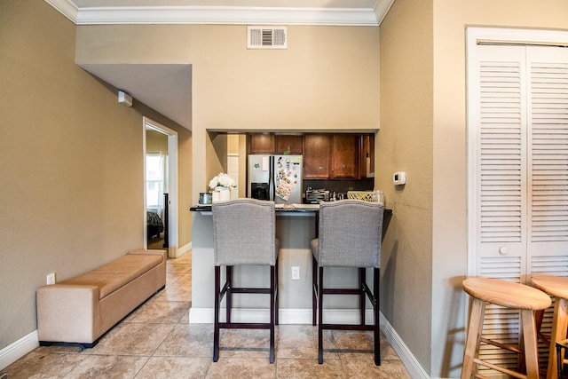 kitchen featuring fridge with ice dispenser, ornamental molding, a kitchen bar, a peninsula, and baseboards