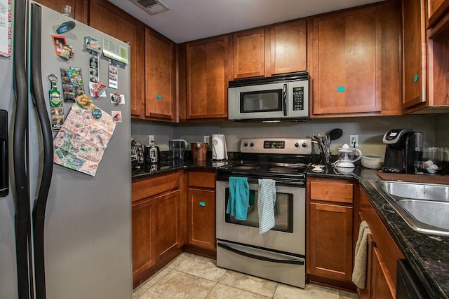 kitchen featuring stainless steel appliances, light tile patterned flooring, brown cabinetry, and a sink