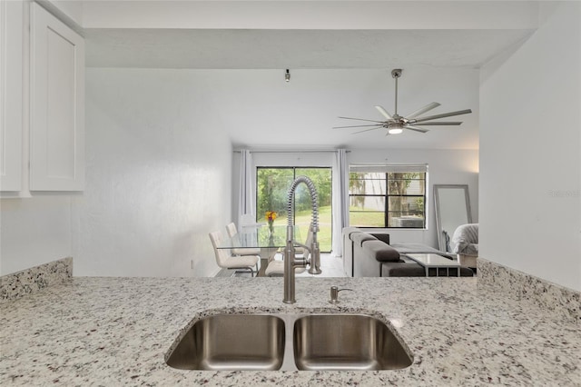 kitchen featuring a sink, light stone countertops, ceiling fan, open floor plan, and white cabinets