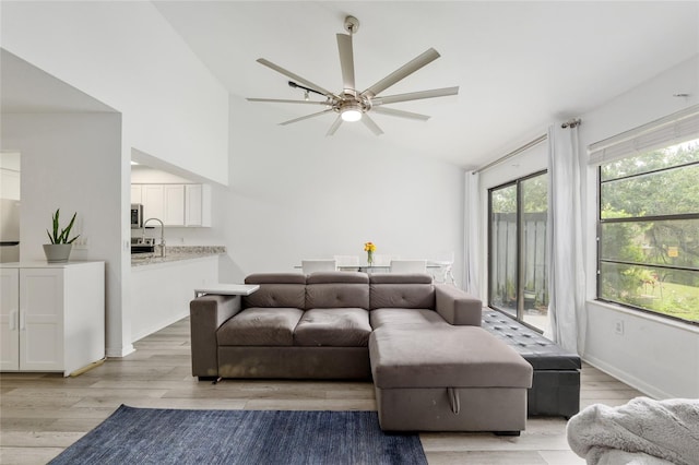 living room with light wood finished floors, ceiling fan, high vaulted ceiling, and baseboards